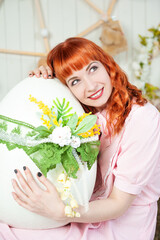 Naklejka premium Cheerful redhead woman hugging a beautifully decorated Easter egg with floral lace details