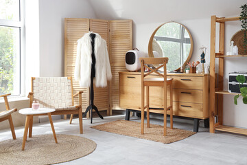 Stylish interior of light room with dressing table, wooden folding screen and mannequin