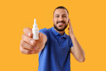 Young man with ear drops on yellow background, closeup