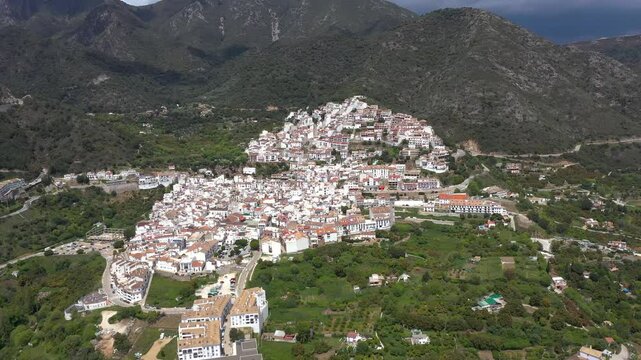 Panoramic aerial perspective of Ojen Village. White Spanish village situated on top of the mountains sourrounded by agriculture fields. Famous travel destination. Rural scene. Drone forward tilt down