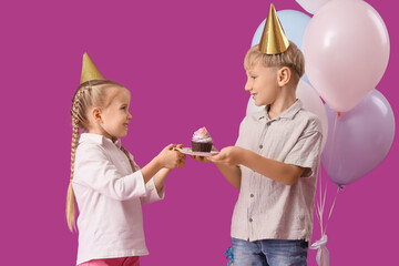 Cute little happy kids in party hats with birthday cupcake and balloons on purple background