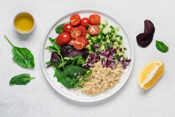 Quinoa salad with tomatoes, lettuce leaves, cucumber, onion in plate on white background with copy space