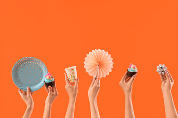 Many female hands with birthday cupcakes and disposable tableware on orange background