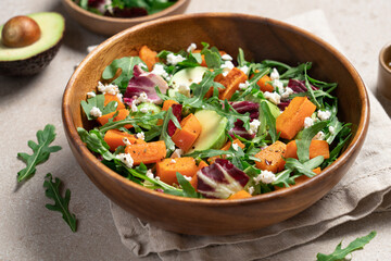 Sweet potato salad with arugula, avocado, cucumber and veta cheese in wooden bowl on light...