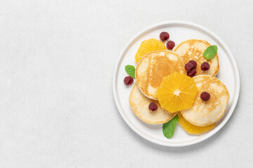 Pancakes with orange and raspberries in plate top view on white background with copy space