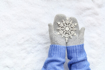 Female hands in warm mittens with beautiful decorative snowflake on snow