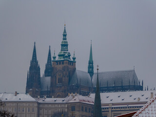 Stunning winter scene of St. Vitus Cathedral in Prague, Czechia. The Gothic cathedral, with its intricate spires and towers, is covered in a blanket of snow, creating a magical and serene atmosphere