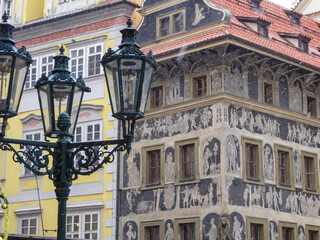 Picturesque scene from Prague, Czech Republic. The focus is on a beautifully decorated building with a facade adorned with intricate murals and sculptures. In the foreground, a vintage street lamp