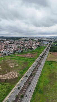 V&iacute;deo com vis&atilde;o a&eacute;rea vertical da Avenida M&aacute;rio Covas J&uacute;nior em Aruj&aacute;, SP, mostrando a movimenta&ccedil;&atilde;o de ve&iacute;culos, a paisagem urbana e o tr&aacute;fego intenso na principal via da cidade