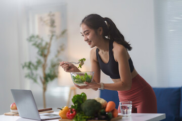 Young asian sportswoman enjoying healthy meal while watching online tutorials on laptop, promoting...