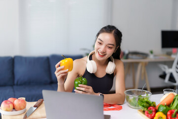 Asian nutritionist holding bell peppers while giving online fitness and health consultation via video call