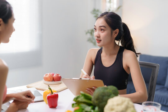 Young nutritionist writing a personalized meal plan during a consultation with a client, promoting healthy eating habits and recommending fresh vegetables