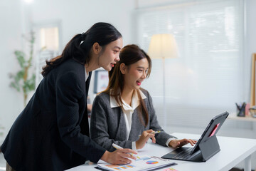 Two asian businesswomen are collaborating on a project, using a convertible laptop to analyze data...