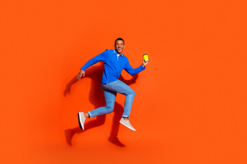Energetic young man in casual blue shirt jumps against an orange backdrop