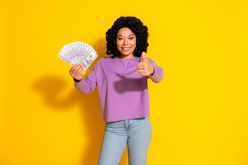 Portrait of pretty young girl money thumb up empty space wear violet pullover isolated on yellow color background