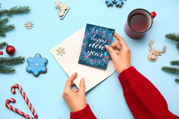 Female hands with envelope, card, cup of tea and Christmas decorations on color background, closeup