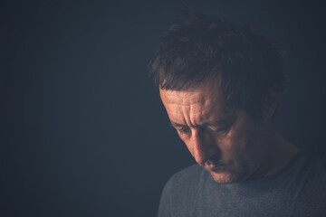 Unhappy contemplative mature adult man thinking in dark room, depressed sulking male pondering