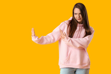 Beautiful young frowning woman rejecting something on yellow background