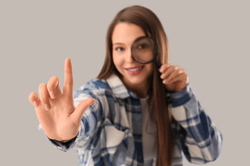 Beautiful happy young woman with raised index finger and magnifier on grey background