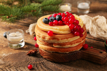 Plate of sweet pancakes with berries burning candles and Christmas tree branch on wooden background
