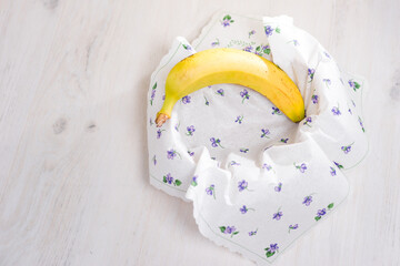 A single, ripe yellow banana rests in a white napkin adorned with small purple flowers. The napkin...