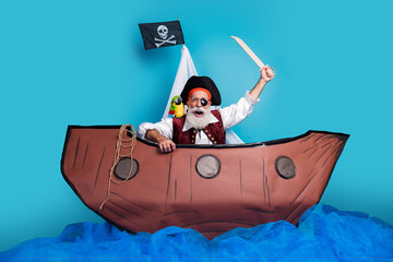 Photo of funny pirate wearing traditional costume swimming in the sea wooden boat isolated on blue color background