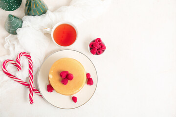 Plate of sweet pancakes with berries, Christmas candy canes and cup of tea on white background