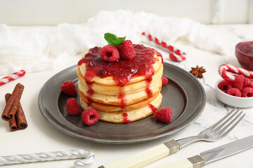 Plate of sweet pancakes with raspberry jam and Christmas candy canes on white background
