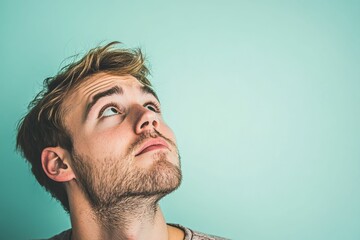 Obraz premium Young man, light stubble, gazing upward, teal background.