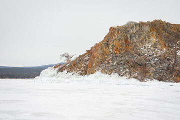 The sky is cloudy and the sun is setting, creating a moody atmosphere. View of Mount Shamanka, Lake Baikal in winter