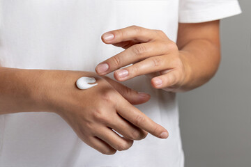 Woman in white t-shirt applying cream on hand to care and protect skin closeup