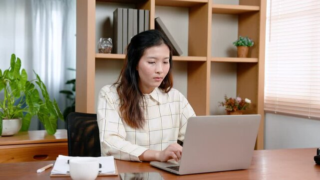 Beautiful Asian woman working in private room in office, sitting typing on laptop computer, sitting working diligently, eyes staring at computer screen, expression serious about work.