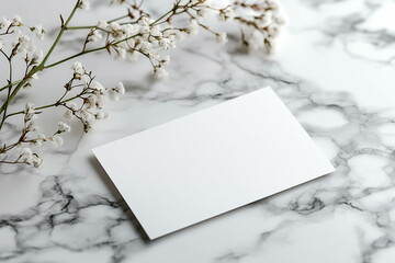 A blank white card placed on a marble surface, surrounded by delicate white flowers. The scene is minimalistic and elegant, ideal for invitations or personal messages.