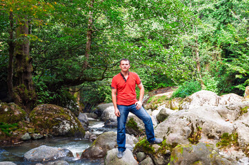 Young man standing confidently on rocks near a rushing mountain river in nature.