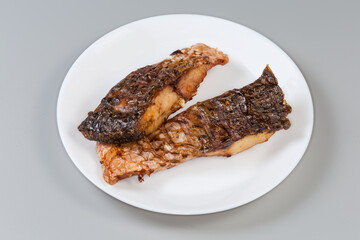 Grilled pieces of carp on white dish on gray background