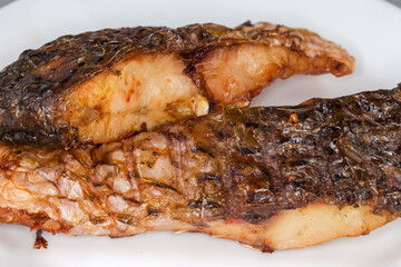 Grilled pieces of carp on white dish, fragment close-up