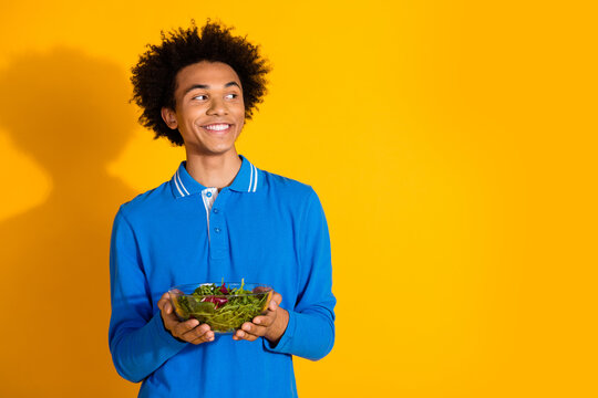 Photo of nice young man hold salad look empty space wear blue shirt isolated on yellow color background