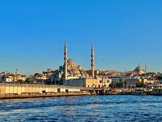 Obraz premium This image shows a scenic view of a waterfront area featuring a prominent mosque with two tall minarets and a large central dome. Surrounding the mosque is a densely built urban area with various 