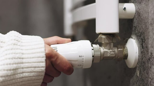 A hand adjusting the heating radiator as cold weather sets in, seeking warmth and comfort at home. A concept highlighting seasonal changes, home heating, and energy efficiency for winter.
