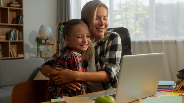Happy Caucasian parent mother speak teach glad daughter little child kid how to use laptop woman help homework online at home family success female clap hands pupil girl high five schoolgirl hug mom
