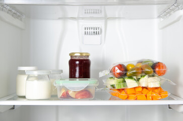 Concept of food preservation in the fridge. Fruits, vegetables in plastic bags and container and yoghurt and jam in jars. 
