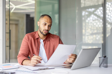 Naklejka premium Business person analyzing paperwork on desk with laptop in a contemporary office environment, demonstrating focus and productivity.