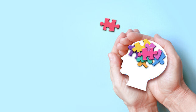 Hands holding paper head with jigsaw puzzle, Autism spectrum disorder family support concept, World Autism Awareness Day