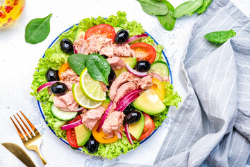 Healthy fat salad with tuna, avocado, olives, vegetables, lettuce and lime. White background, top view