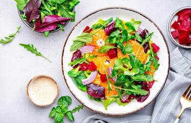 Vegan salad with baked beets, tangerine, red onion, lettuce, sesame and arugula, gray background, top view