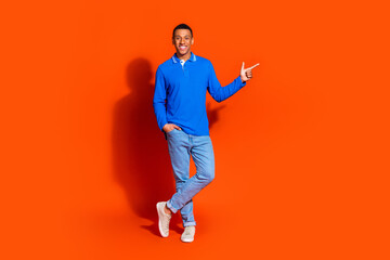 Young man in blue sweater points confidently against orange background
