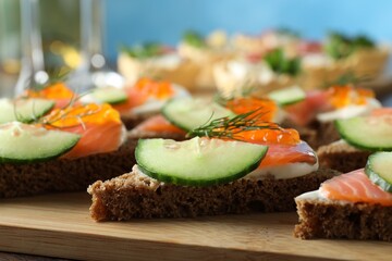 Tasty canapes with salmon and cucumber on wooden table, closeup