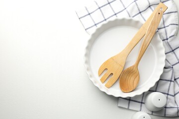 Ceramic casserole and other cooking utensils on white table, top view. Space for text