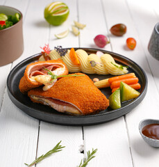 cordon bleu chicken With cheese and herbs, next to mashed potatoes, assortment of side dishes, white wooden background