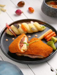 cordon bleu chicken With cheese and herbs, next to mashed potatoes, assortment of side dishes, white wooden background